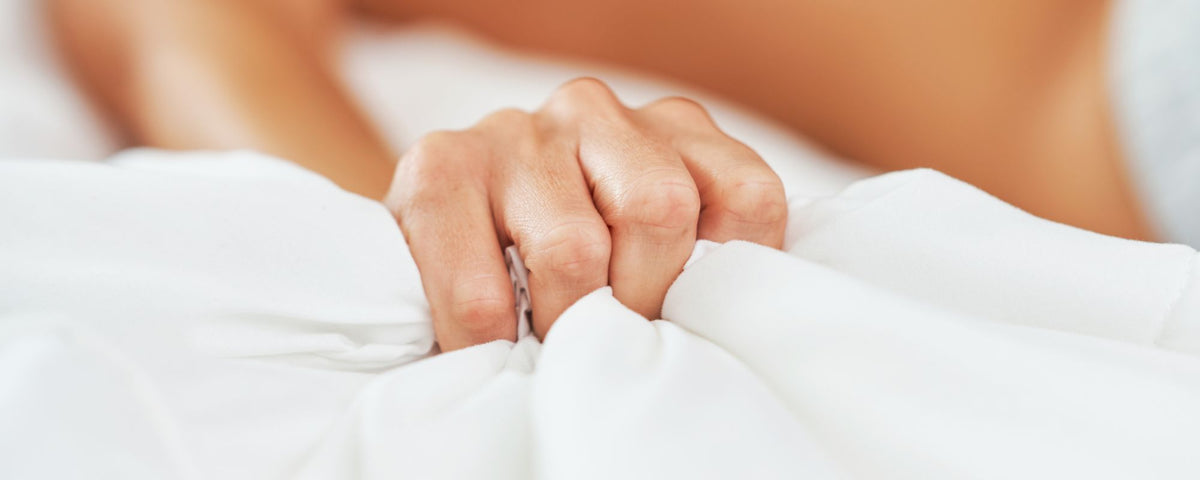 a man reaching climax in bed behind white sheets